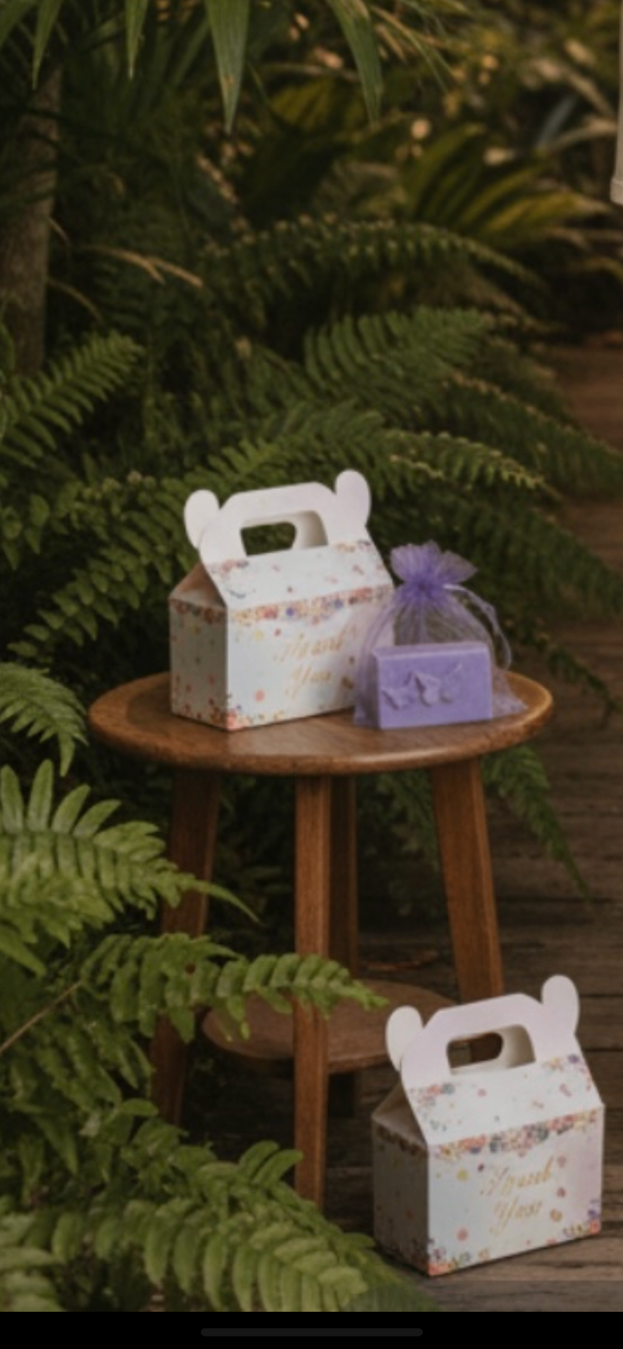 Floral thank-you gift boxes with a lavender butterfly soap on a wooden stool among tropical ferns