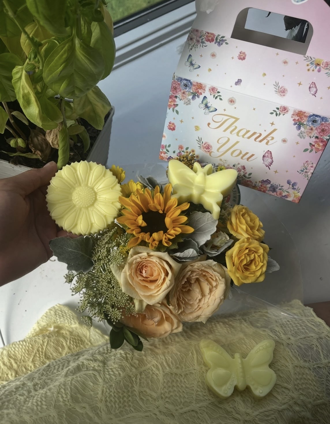 Golden yellow butterfly and sunflower soaps held beside a sunflower and rose bouquet with a floral thank-you box