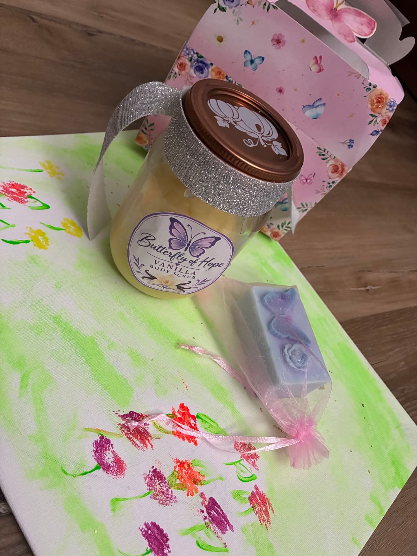 A glass jar of Butterfly of Hope vanilla body scrub with a butterfly soap in a keepsake bag