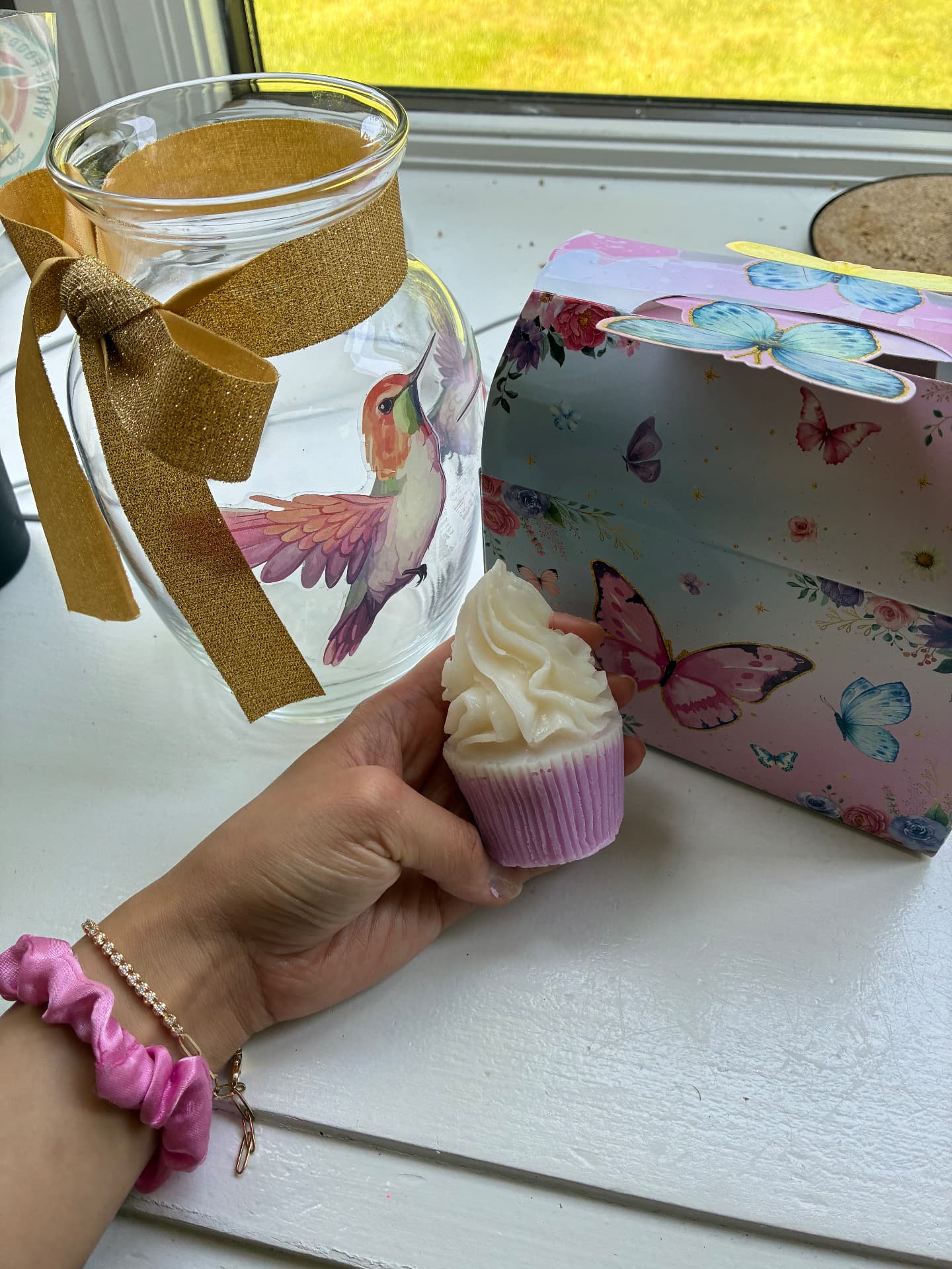 Milestone cupcake soap held beside a butterfly-print gift box and hummingbird jar