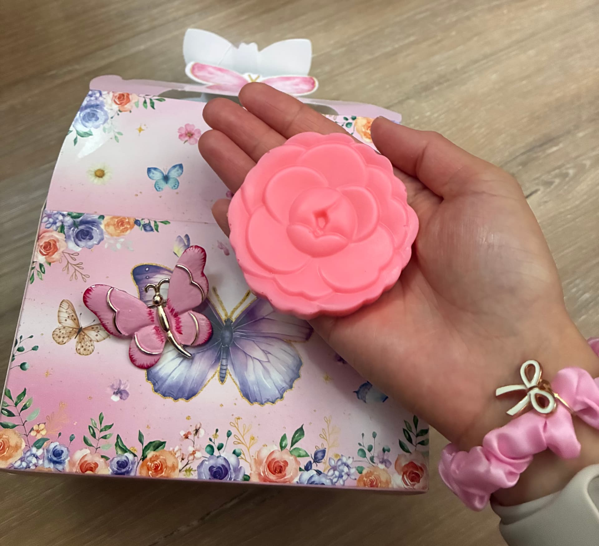 A hand holding a blush rose-shaped soap next to a butterfly-themed gift box