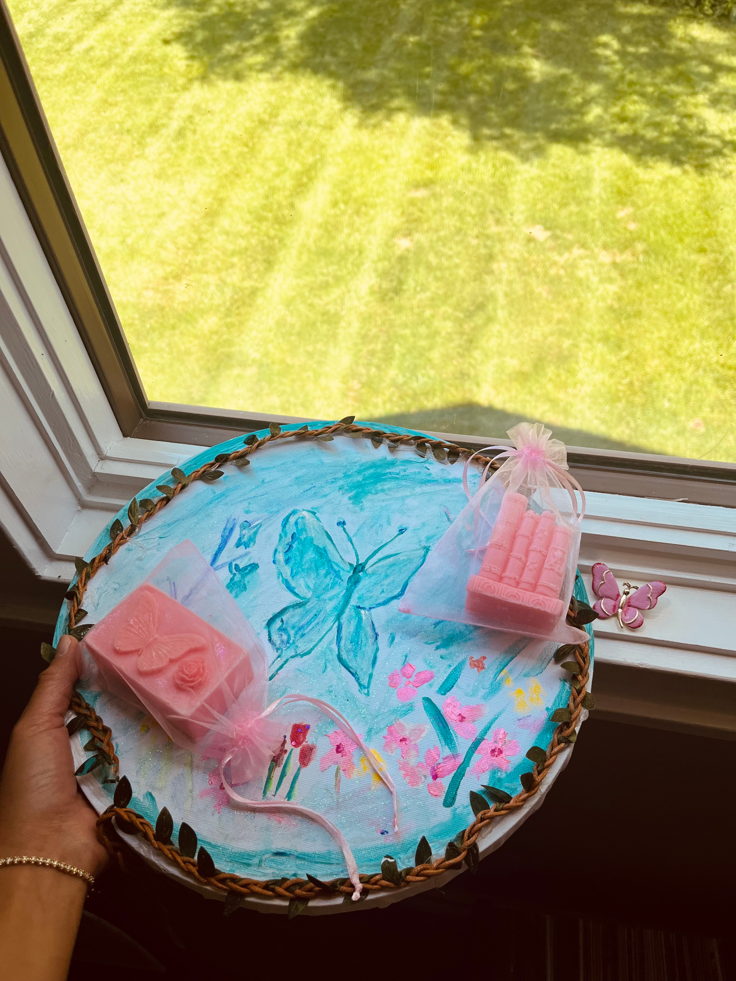 Pink butterfly and book-stack soaps resting on a hand-painted tray of butterflies and wildflowers, made by a survivor